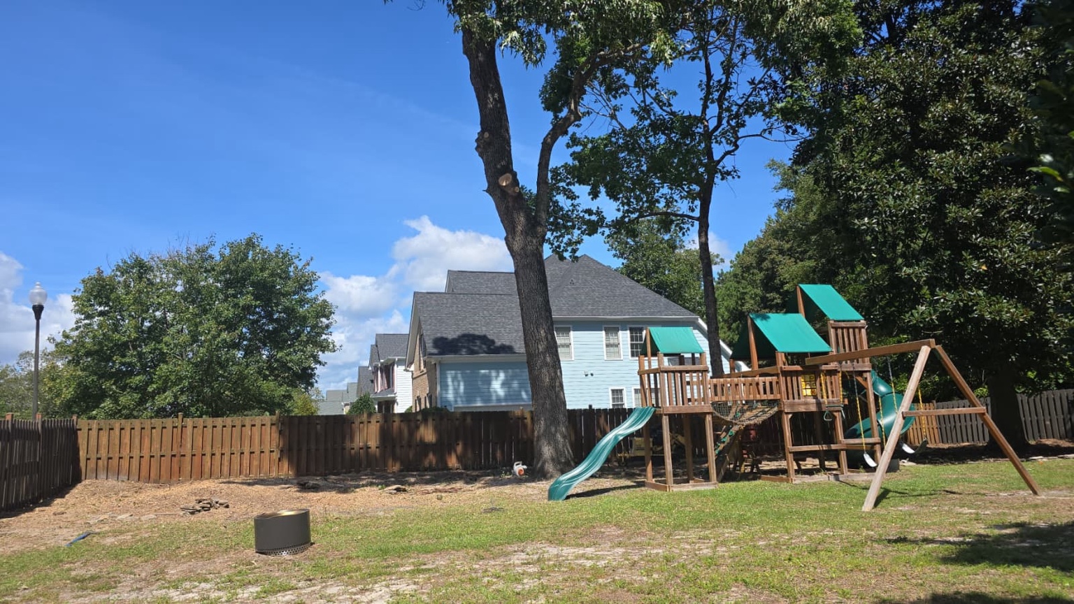 Large backyard tree removal project beside a house, fence, and children's playset